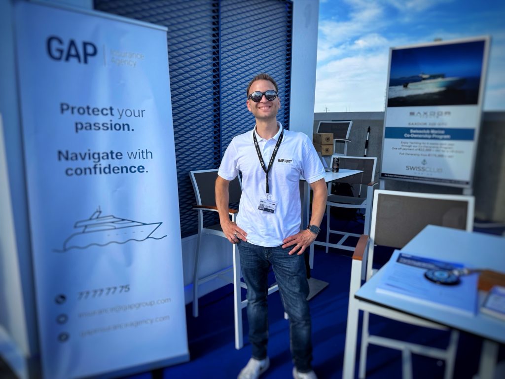 George Karapateas smiling and posing in front of a GAP Insurance Agency banner at an outdoor exhibition booth during the Limassol Marina Boat Show 2025.