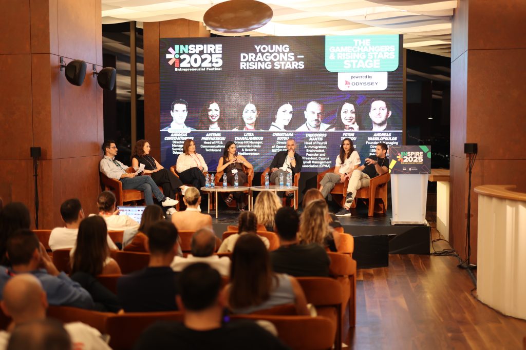 A panel of seven speakers on stage at Inspire 2025 Entrepreneurial Festival in Nicosia, Cyprus. The backdrop screen shows the session title “Young Dragons – Rising Stars” and names of the speakers. Andreas Vassilopoulos is seated at the right end, participating in the discussion.